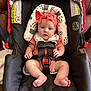 baby, car_seat, headband, bow, straps, infant, indoors, face, hands, feet, cushion, pattern, clothing, sitting, leather, safety, child, expression, seatbelt, closeup