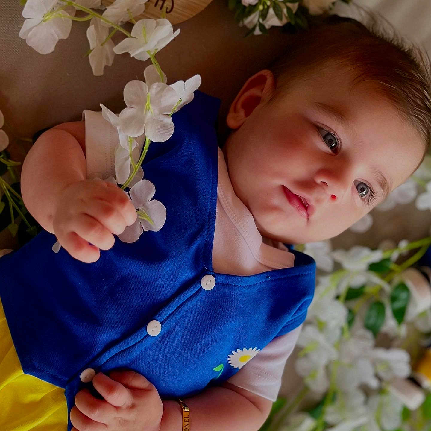 Leonel is registered to the contest to win money with this photo: baby, background, blue_vest, bracelet, child, cute, eyes, face, flower, hand, infant, lying_down, milestone_sign, peaceful, portrait, skin, soft_lighting, white_flower, wooden_sign, yellow_pants