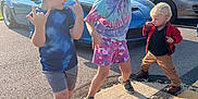 Caden is registered to the contest to win money with this photo: child, children, boy, girl, toddler, parking_lot, car, sports_car, sunny, daylight, asphalt, cap, shorts, sneakers, jacket, playful, posing, outdoor, fun, smiling