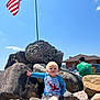 toddler, child, rocks, flag, american_flag, sky, outdoor, sunny, person, man, woman, building, car, clothing, shorts, shirt, pointing, blonde_hair, nature, casual