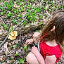 child, red_shirt, forest, mushrooms, leaves, fallen_branch, green_plants, outdoor, nature, curly_hair, kneeling, purple_shoe, exploration, woodland, ground, plants, casual_clothing, daylight, person, crouching