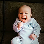 Isaac participe au concours pour gagner de l'argent avec cette photo : baby, infant, smiling, happy, onesie, penguin, couch, furniture, seated, child, cute, indoor, portrait, young, joyful, clothing, person, expression, hands, face