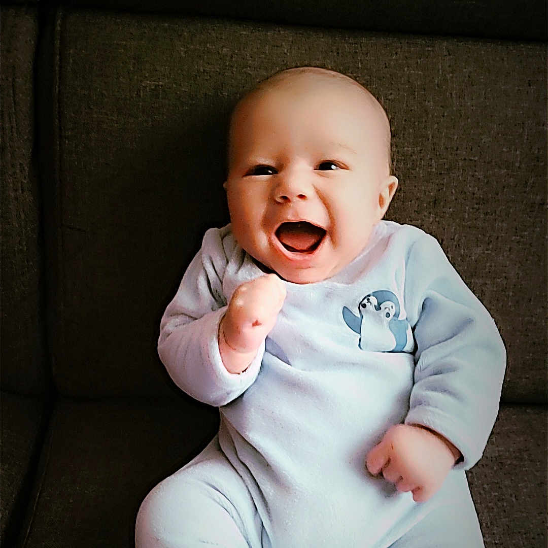Isaac participe au concours pour gagner de l'argent avec cette photo : baby, child, clothing, couch, cute, expression, face, furniture, hands, happy, indoor, infant, joyful, onesie, penguin, person, portrait, seated, smiling, young