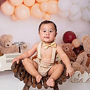 Sebastian joined the competition — help win amazing prizes! baby, child, teddy_bear, balloon, chair, bow_tie, suspenders, wooden_chair, plush_toy, party_decor, smiling, cute, indoor, portrait, person, celebration, baby_clothing, floor, background, happy