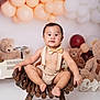 baby, child, teddy_bear, balloon, chair, bow_tie, suspenders, wooden_chair, plush_toy, party_decor, smiling, cute, indoor, portrait, person, celebration, baby_clothing, floor, background, happy