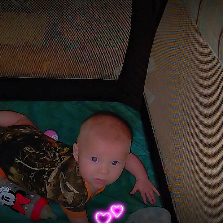 Rosalyn is registered to the contest to win money with this photo: baby, playpen, crawling, camouflage_clothing, blanket, toy, mickey_mouse, indoor, child, infant, cute, heart_sticker, curious, floor, soft_surface, pajamas, person, head, eyes, hands