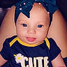 baby, headband, blue, shirt, text, cute, child, smiling, tongue_out, freckles, indoor, person, sitting, flower_graphic, navy_blue, yellow, infant, playful, closeup, portrait