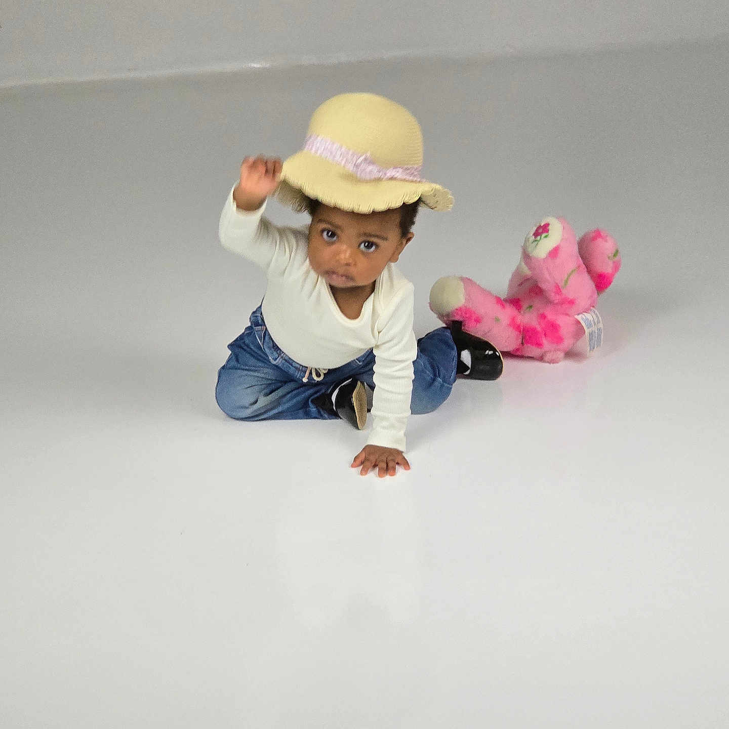 Anatswa joined the competition — help win amazing prizes! black_shoes, blue_jeans, child, curious, cute, expression, floor, hat, indoor, minimalist, pink_stuffed_animal, playful, portrait, sitting, studio, toddler, toy, white_shirt, yellow_hat, young_child