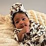 adorable, baby, blanket, child, cozy, curious, cute, expression, face, headwrap, indoors, infant, leopard_print, lying_down, portrait, skin, small_hand, soft_texture, warm_clothing, young