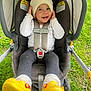 baby, child, stroller, hat, yellow_shoes, smiling, happy, outdoor, grass, baby_clothing, car_seat, infant, cute, playful, person, legs, feet, headwear, sitting, baby_accessory
