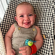 Camille a rejoint le concours — aidez-le/la à gagner de superbes lots ! baby, smiling, child, wrist_toy, romper, cushion, checkered_pattern, happy, indoor, infant, person, cute, seated, close_up, skin, playful, bright, eyes, hand, soft_fabric