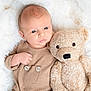 baby, infant, teddy_bear, plush_toy, blanket, soft_texture, beige_clothing, cute, child, lying_down, portrait, indoor, comfort, warmth, sleepy, adorable, cozy, newborn, cuddly, peaceful