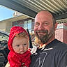 baby, man, beard, red_hoodie, polka_dots, outdoor, car, building, metal_canopy, smile, portrait, holding, child, casual_clothing, daylight, facial_expression, person, headwear, window, door