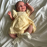Bonnie is registered to the contest to win money with this photo: baby, infant, smile, dress, yellow_dress, socks, white_socks, lying_down, bed_sheet, white_sheet, cute, happy, newborn, child, portrait, soft_lighting, indoors, wrinkles, fabric, skin