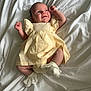 baby, infant, smile, dress, yellow_dress, socks, white_socks, lying_down, bed_sheet, white_sheet, cute, happy, newborn, child, portrait, soft_lighting, indoors, wrinkles, fabric, skin
