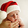 baby, santa_hat, red_hat, white_fur, face, hand, skin, closeup, expression, cute, child, infant, portrait, holiday, christmas, soft_light, neutral_background, holding, pensive, young