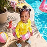 toddler, child, poolside, swimsuit, inflatable_ring, heart_shaped_sunglasses, beach_ball, flamingo_float, summer, sunny, outdoor, potted_plant, lounge_chair, drink, shadow, concrete, smiling, playful, water, footwear