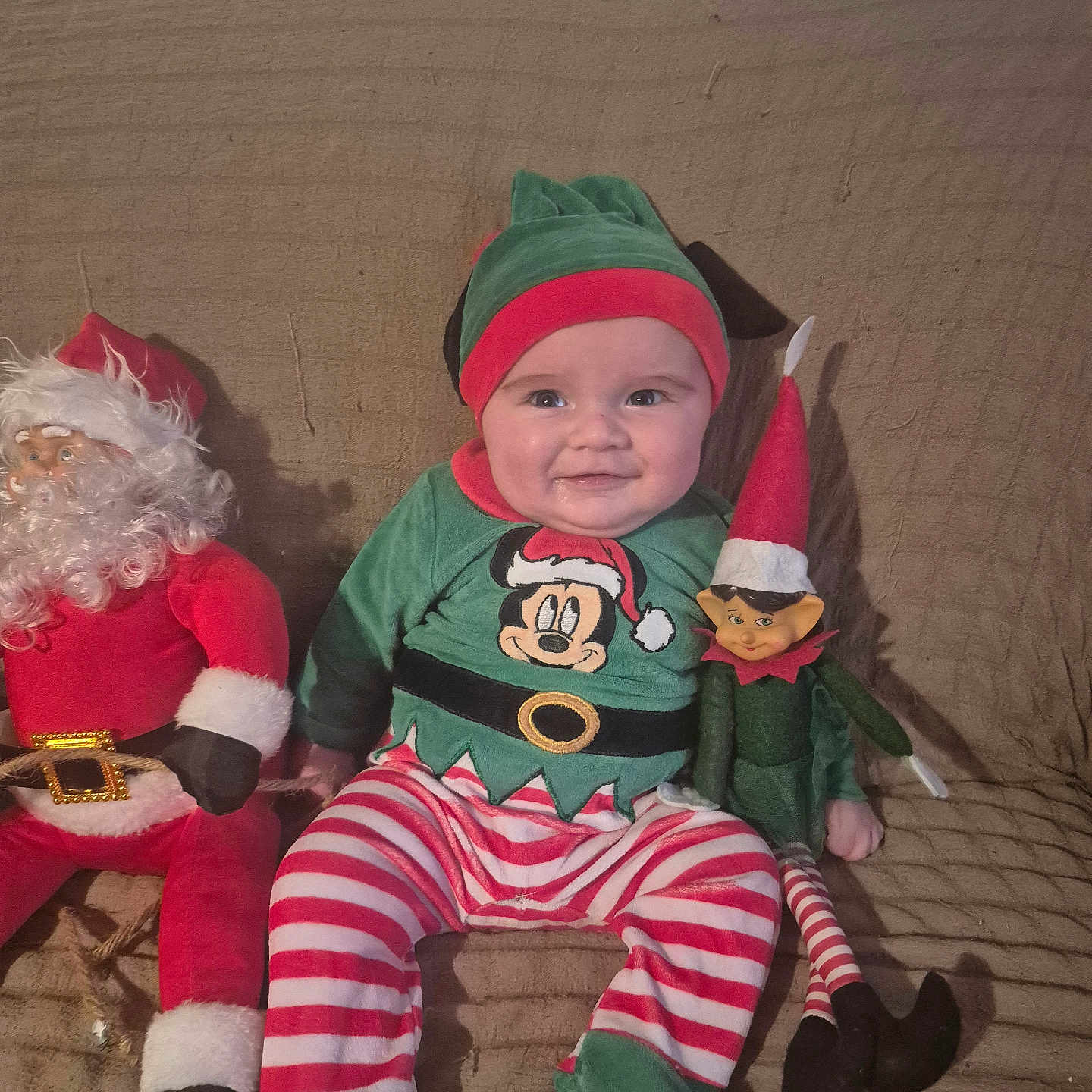 Owen participe au concours pour gagner de l'argent avec cette photo : baby, child, christmas, couch, cozy, cute, elf_doll, elf_hat, festive_clothing, green, happy, holiday, indoor, person, plush_toy, red, santa_claus_doll, seated, smile, striped_pants