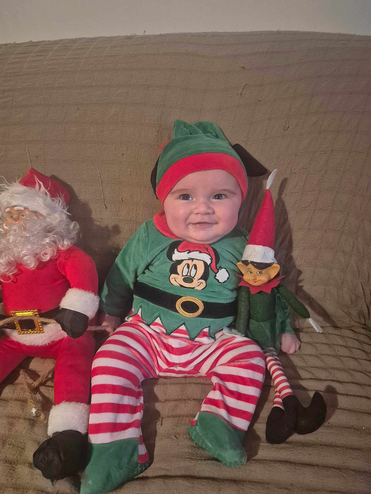 Owen participe au concours pour gagner de l'argent avec cette photo : baby, child, smile, festive_clothing, elf_hat, striped_pants, plush_toy, santa_claus_doll, elf_doll, couch, indoor, holiday, christmas, happy, cute, person, seated, cozy, red, green