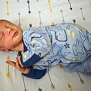 Ryland is registered to the contest to win money with this photo: baby, newborn, sleeping, onesie, blue_clothing, blanket, arrows, pattern, infant, peaceful, cute, child, lying_down, soft, toddler, face, hand, footed_pajamas, indoors, resting