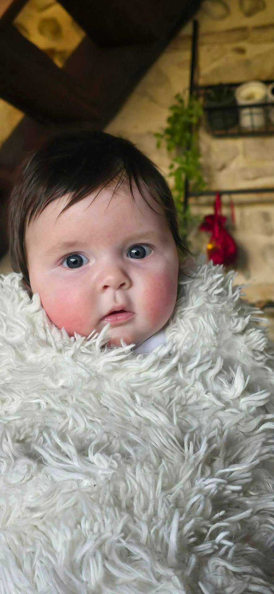 Raphaëlle a rejoint le concours — aidez-le/la à gagner de superbes lots ! baby, child, face, blanket, fluffy, indoor, portrait, curious, rosy_cheeks, dark_hair, cozy, warm, candid, closeup, person, soft_texture, expression, young, wrapped, infant