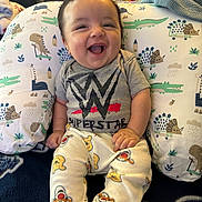Demetrius is registered to the contest to win money with this photo: baby, smiling, sitting, wwe_superstar_shirt, winnie_the_pooh_pajamas, cushion, dinosaur_print, indoor, happy, child, cute, infant, clothing, face, hand, blanket, furniture, portrait, young_child, home