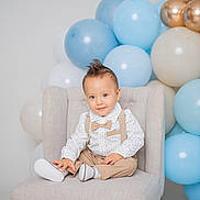 Justin is registered to the contest to win money with this photo: toddler, child, balloons, chair, suspenders, bow_tie, polka_dot, shirt, beige, blue, gold, celebration, party, portrait, smiling, hair, indoor, cute, fashion, seated