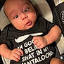 Jermaine is registered to the contest to win money with this photo: baby, infant, onesie, black_clothing, text_on_clothing, cushion, car_seat, warning_label, hands, legs, face, eyes, skin, child, cute, expression, indoor, newborn, seat, clothing