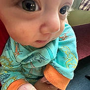 Jermaine is registered to the contest to win money with this photo: baby, close_up, dinosaur_print, clothing, hand, infant, face, eye, colorful, orange_cuffs, indoor, person, child, cute, young, patterned, fabric, soft, skin, apparel
