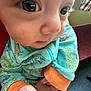 baby, close_up, dinosaur_print, clothing, hand, infant, face, eye, colorful, orange_cuffs, indoor, person, child, cute, young, patterned, fabric, soft, skin, apparel