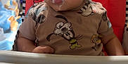 Jermaine is registered to the contest to win money with this photo: baby, cartoon_shirt, child, clothing, curious, cute, expression, face, feeding, furniture, high_chair, home, indoor, messy, milk, person, table, television, toy, young