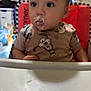 baby, cartoon_shirt, child, clothing, curious, cute, expression, face, feeding, furniture, high_chair, home, indoor, messy, milk, person, table, television, toy, young