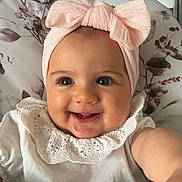 Romane participe au concours pour gagner de l'argent avec cette photo : baby, child, smile, headband, pink, white_clothing, lace, face, arm, hand, indoor, cushion, floral_pattern, highchair, happy, infant, portrait, cute, person, closeup
