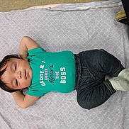 Echo is registered to the contest to win money with this photo: baby, blanket, clothing, dark_pants, face, feet, floor, footwear, happy, infant, jeans, lying_down, person, portrait, resting, shirt, socks, text_on_clothing, young_child, indoor
