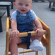 Keyden participe au concours pour gagner de l'argent avec cette photo : baby, baby_clothing, child, cute, daylight, denim_overalls, face, footwear, hands, happy, high_chair, infant, legs, outdoor, person, seat, smiling, tiled_floor, white_sneakers, wooden_chair