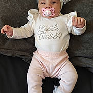 Aaliyah is registered to the contest to win money with this photo: baby, infant, pacifier, headband, bow, white_clothing, pink_pants, socks, ruffles, cute, lying_down, face, child, adorable, text_on_clothing, indoor, soft_texture, sleepwear, newborn, smiling