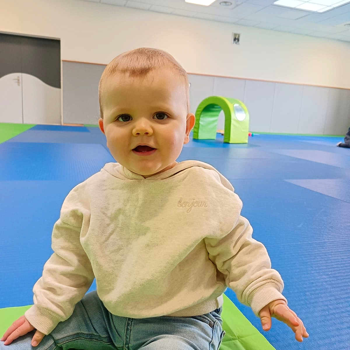 Lenny a rejoint le concours — aidez-le/la à gagner de superbes lots ! toddler, child, indoor, play_area, mat, blue_floor, green_tunnel, casual_clothing, jeans, hoodie, smiling, sitting, cute, young_child, play, fun, bright, daylight, person, portrait
