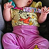 baby, infant, car_seat, pacifier, clothing, pink_pants, yellow_shirt, winnie_the_pooh, cute, child, small_feet, sitting, indoors, safety_harness, person, portrait, head, face, hand, foot