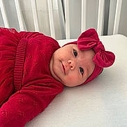 Izabella is registered to the contest to win money with this photo: baby, infant, red_clothing, headband, bow, crib, white_bed, cute, portrait, child, smile, lying_down, soft_lighting, indoors, toddler, face, person, apparel, cozy, sleeping_area