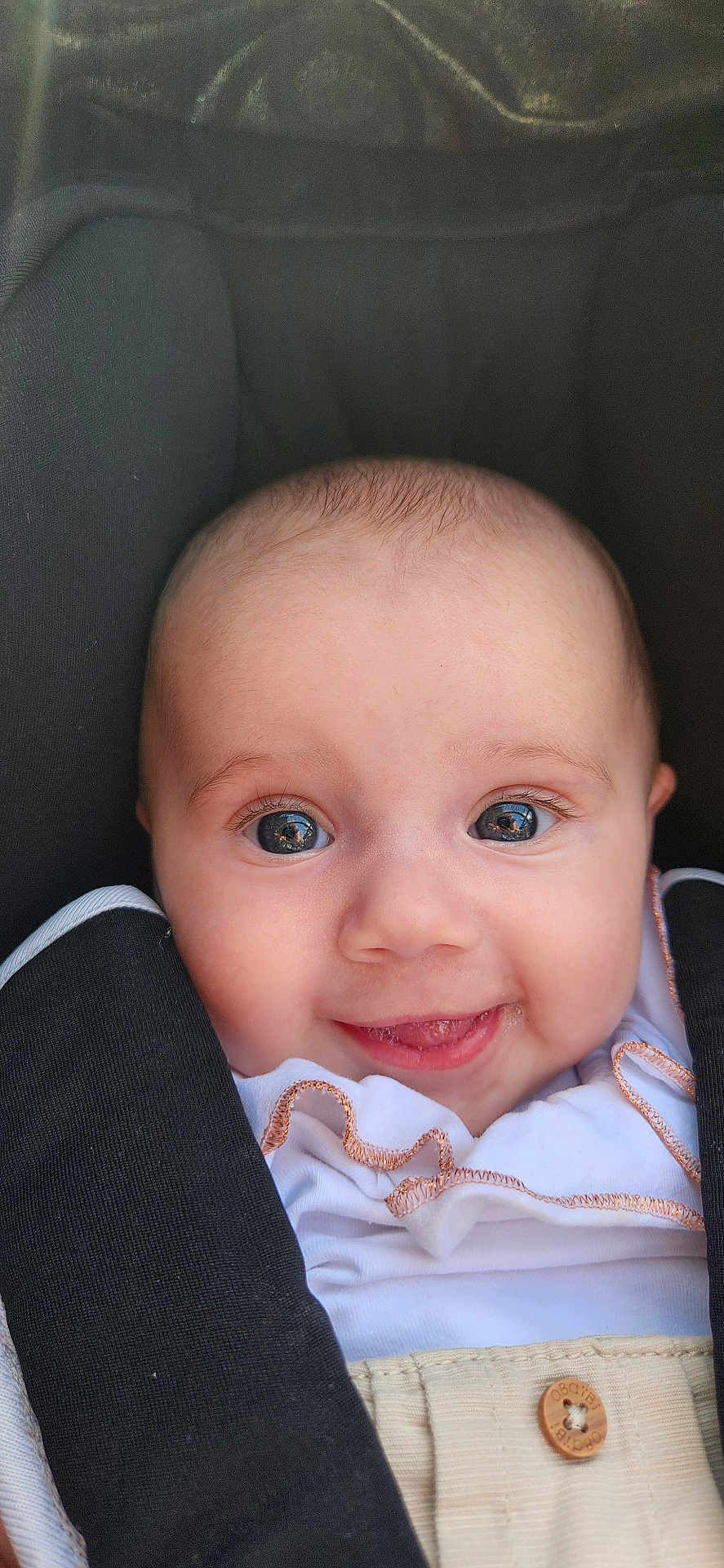 Olivia participe au concours pour gagner de l'argent avec cette photo : baby, infant, face, smile, eyes, car_seat, clothing, white_shirt, black_strap, cute, child, young, portrait, close_up, happy, skin, head, button, seatbelt, babywearing