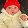 baby, infant, red_hat, pom_pom, white_jacket, fluffy_clothing, stroller, child, cute, wide_eyes, winter_clothing, face, portrait, curious, hands, warm, outdoor_gear, soft_texture, headwear, closeup