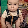 baby, infant, child, sitting, portrait, wide_eyes, looking_at_camera, playroom, indoor, colorful_carpet, playground, slide, soft_play, overalls, beige_shirt, barefoot, pacifier, patterned_rug, centered_composition, candid_photo
