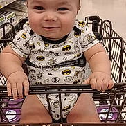 Wyatt is registered to the contest to win money with this photo: baby, child, infant, smiling, portrait, grocery_store, shopping_cart, superhero_clothing, batman, store_aisle, indoors, retail, sitting, hands, bare_legs, cart, shelves, shopping, happy, photograph