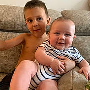 Gabriel a rejoint le concours — aidez-le/la à gagner de superbes lots ! baby, child, sibling, couch, striped_clothing, smile, happy, indoor, portrait, bare_chest, furniture, living_room, person, cute, young_child, infant, family, relaxing, skin, foot