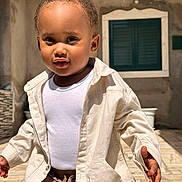Hadriel participe au concours pour gagner de l'argent avec cette photo : toddler, child, outdoor, sunlight, jacket, white_shirt, curly_hair, face, walking, expression, window, wall, pavement, person, young_child, casual_clothing, daytime, portrait, cute, curious