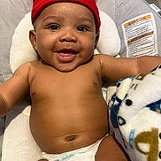 Jason is registered to the contest to win money with this photo: baby, smiling, red_beanie, diaper, blanket, cushion, baby_seat, happy, infant, face, skin, headwear, child, indoor, cute, person, portrait, expression, comfort, young