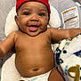 baby, smiling, red_beanie, diaper, blanket, cushion, baby_seat, happy, infant, face, skin, headwear, child, indoor, cute, person, portrait, expression, comfort, young