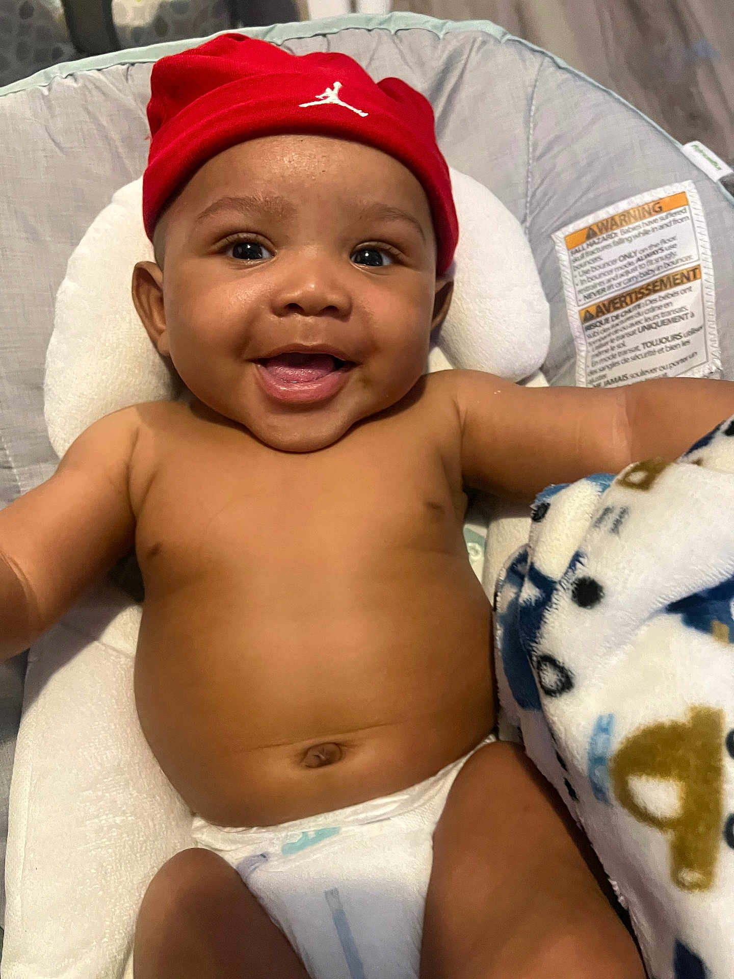 Jason is registered to the contest to win money with this photo: baby, smiling, red_beanie, diaper, blanket, cushion, baby_seat, happy, infant, face, skin, headwear, child, indoor, cute, person, portrait, expression, comfort, young