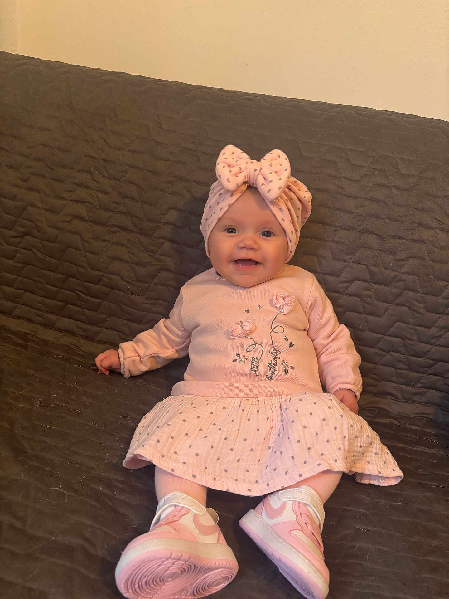 Inaya participe au concours pour gagner de l'argent avec cette photo : baby, infant, child, headband, bow, pink, dress, sneakers, couch, quilted_blanket, smile, happy, portrait, sitting, indoor, clothing, face, eyes, cheeks, legs