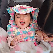Inara joined the competition — help win amazing prizes! baby, child, smiling, hat, colorful_clothing, blanket, indoor, happy, person, face, infant, seated, fabric, playful, car_seat, tissue, pink, white, cute, joyful